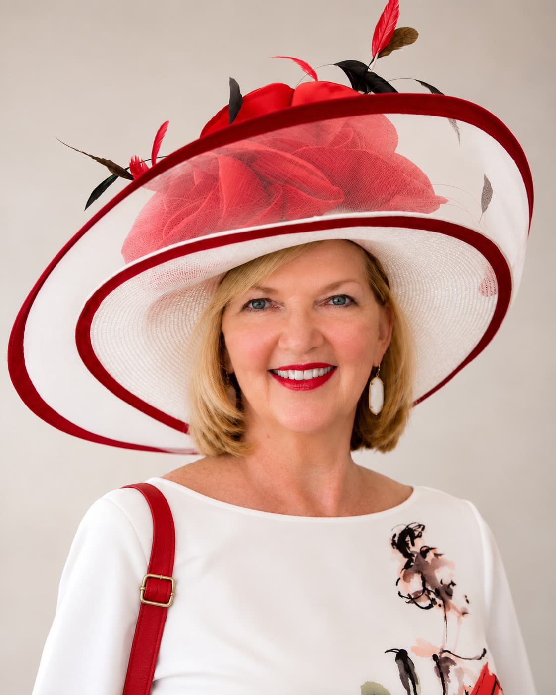 GeorgeAnn Dingus smiling beneath a wide-brimmed white hat trimmed in red, with a red rose and feathers